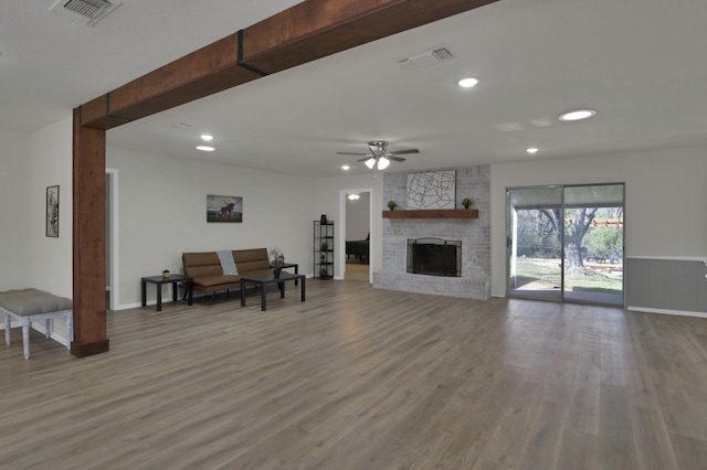 living room with a brick fireplace, ceiling fan, visible vents, and wood finished floors