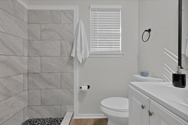bathroom with toilet, tiled shower, and vanity