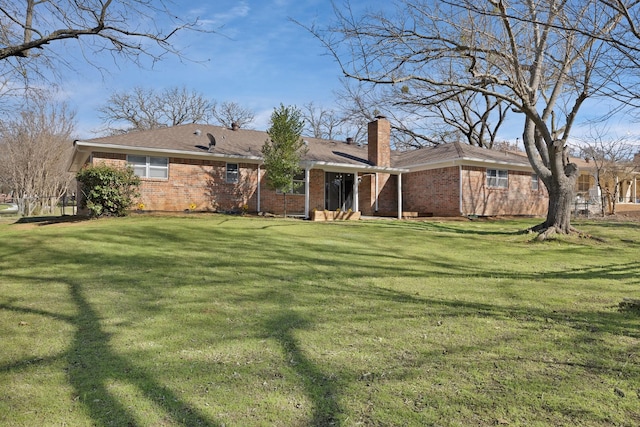 back of house featuring brick siding, a yard, and a chimney
