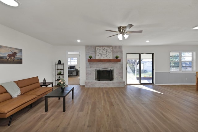 living area featuring a brick fireplace, baseboards, light wood-type flooring, recessed lighting, and a ceiling fan