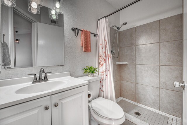 bathroom with toilet, a textured wall, vanity, and a stall shower