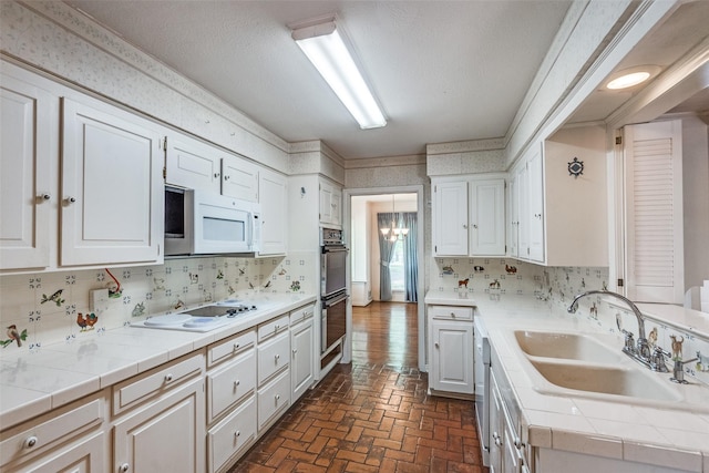 kitchen featuring white cabinets, tile countertops, a sink, white appliances, and brick floor