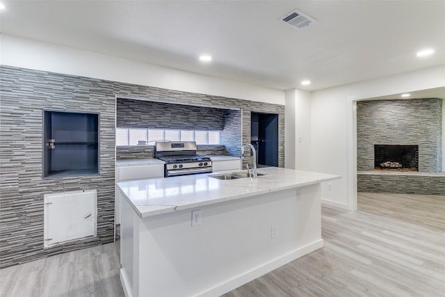 kitchen featuring a sink, visible vents, light wood-style floors, gas range, and a stone fireplace