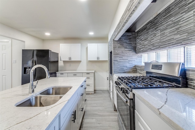 kitchen with stainless steel range with gas stovetop, a sink, black fridge, recessed lighting, and white cabinetry