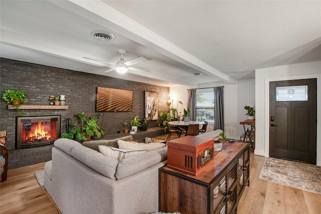 living room featuring beamed ceiling, visible vents, a large fireplace, and light wood-style flooring