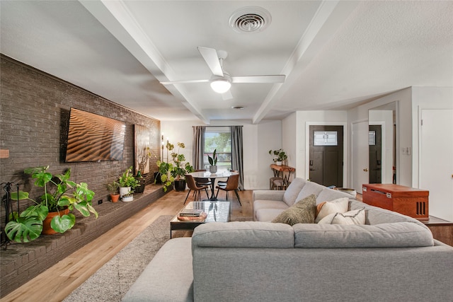 living area with visible vents, wood finished floors, brick wall, beam ceiling, and ceiling fan