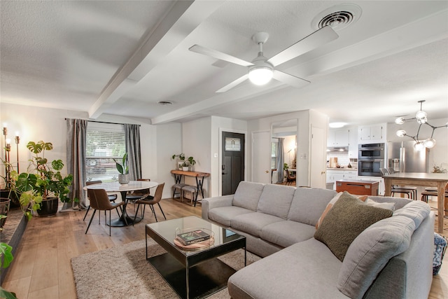 living area with a ceiling fan, beamed ceiling, visible vents, and light wood-type flooring