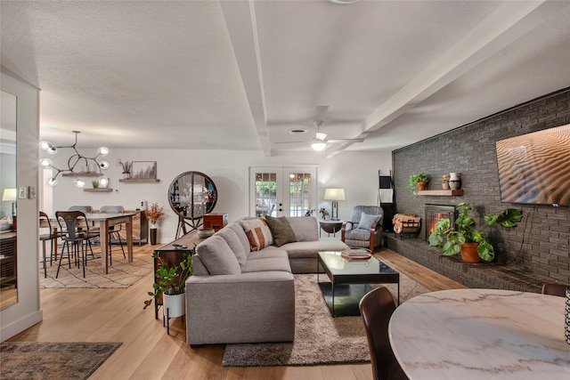 living area featuring a brick fireplace, beam ceiling, brick wall, ceiling fan, and light wood-style flooring