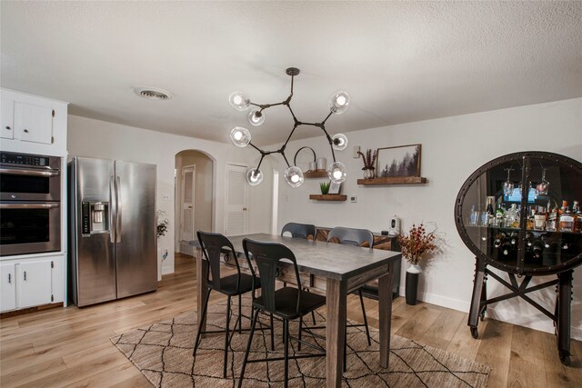 dining room with arched walkways, baseboards, light wood finished floors, and visible vents