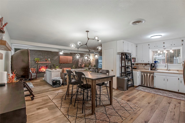 kitchen featuring white cabinets, a sink, light wood-style floors, stainless steel dishwasher, and visible vents