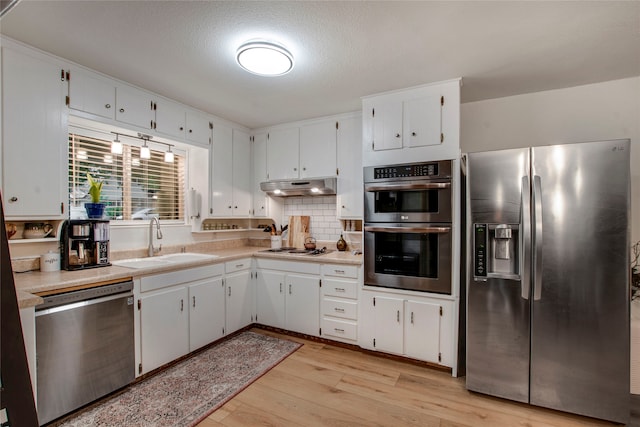 kitchen featuring appliances with stainless steel finishes, a sink, light countertops, under cabinet range hood, and light wood-style flooring
