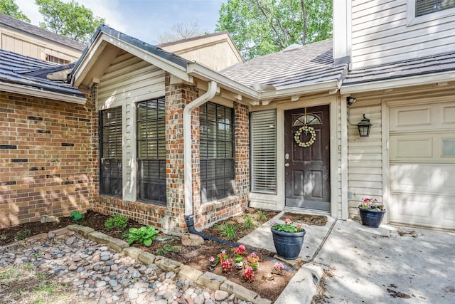 doorway to property with an attached garage, brick siding, and a shingled roof