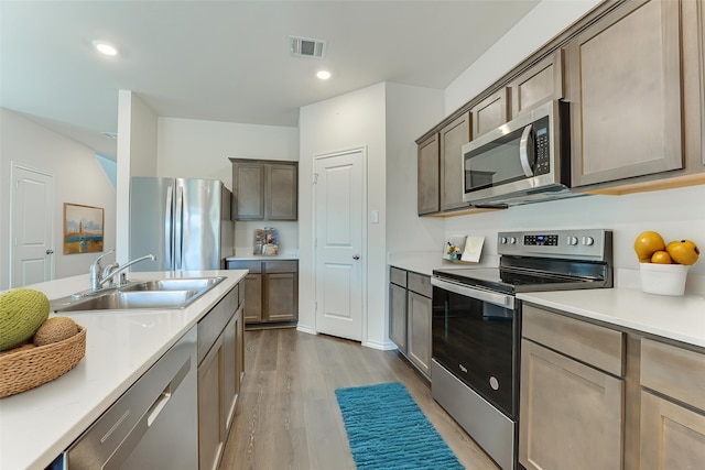 kitchen with stainless steel appliances, light countertops, wood finished floors, visible vents, and a sink