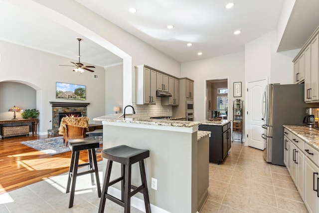 kitchen featuring under cabinet range hood, light tile patterned floors, a fireplace, a kitchen bar, and ceiling fan