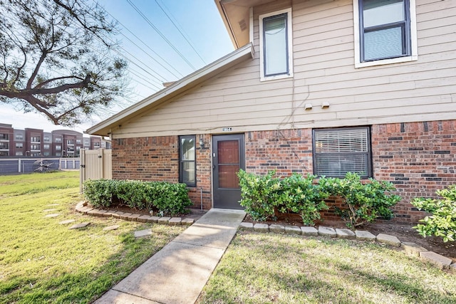 doorway to property with a lawn, fence, and brick siding