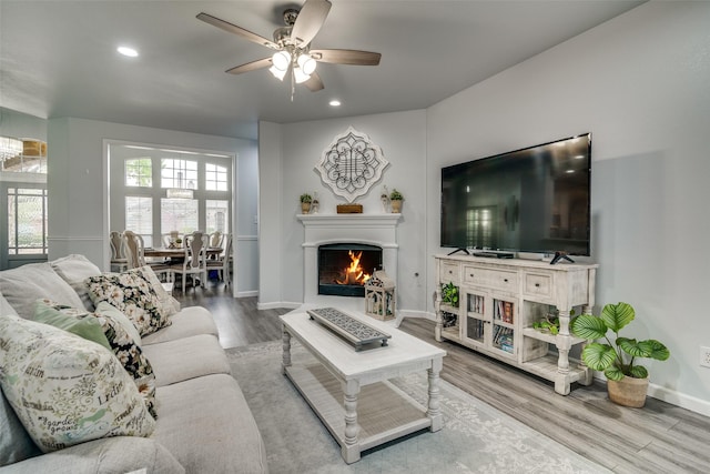 living area with wood finished floors, ceiling fan, a lit fireplace, baseboards, and recessed lighting