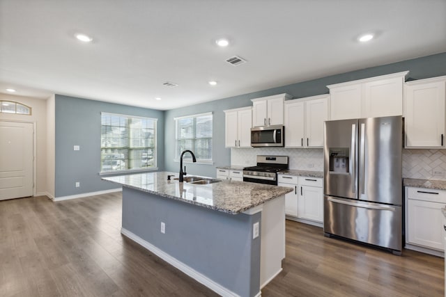 kitchen featuring a center island with sink, white cabinetry, tasteful backsplash, a sink, and appliances with stainless steel finishes