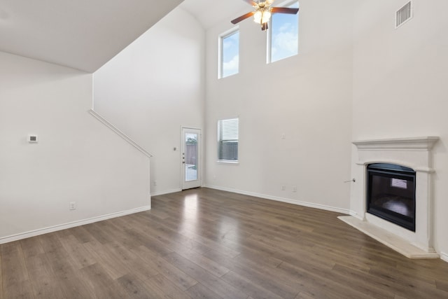 unfurnished living room with ceiling fan, visible vents, wood finished floors, high vaulted ceiling, and a glass covered fireplace