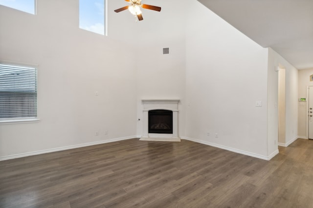 unfurnished living room with ceiling fan, visible vents, wood finished floors, a fireplace with raised hearth, and a high ceiling