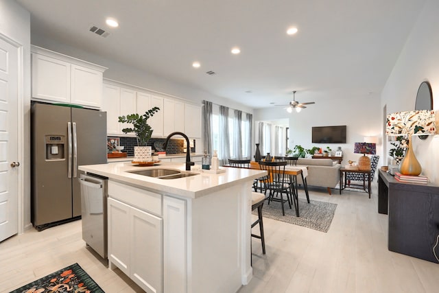 kitchen featuring a ceiling fan, open floor plan, white cabinetry, a sink, and stainless steel appliances