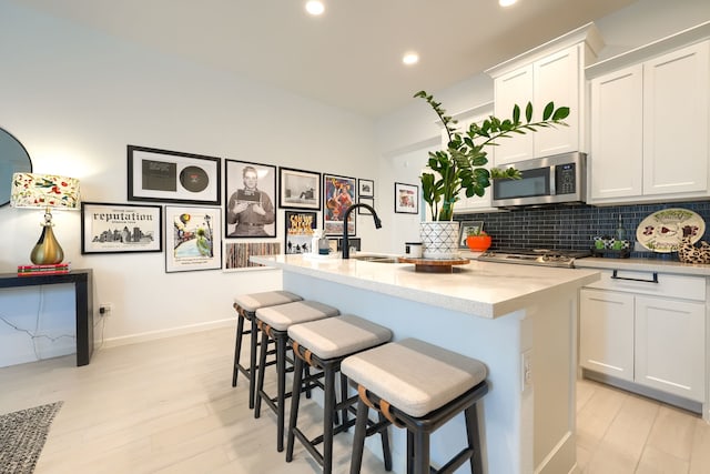 kitchen featuring tasteful backsplash, a center island with sink, a sink, white cabinets, and stainless steel microwave