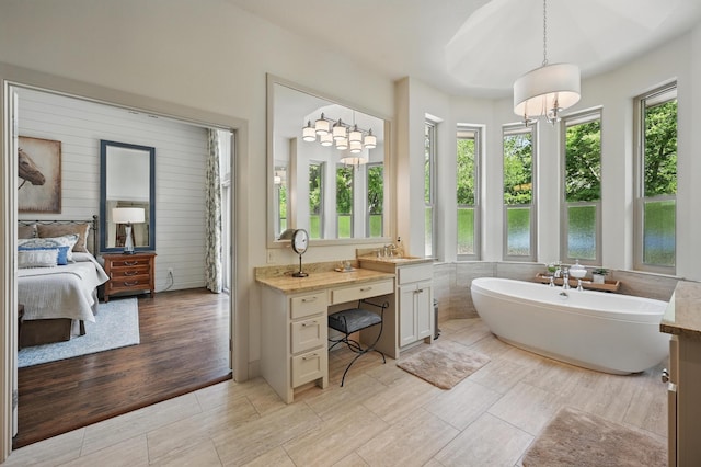 ensuite bathroom featuring ensuite bath, a wealth of natural light, a soaking tub, and vanity