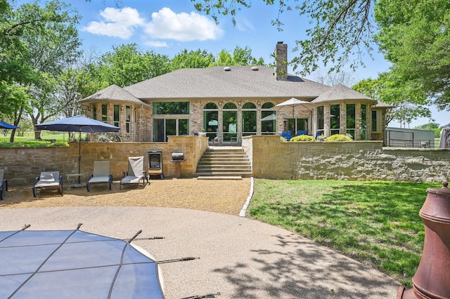 rear view of house featuring roof with shingles, a chimney, brick siding, stairway, and a patio