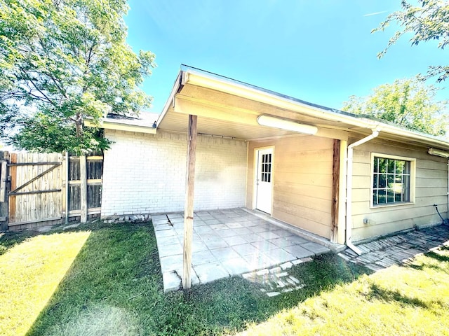 rear view of property with a gate, fence, brick siding, a lawn, and a patio