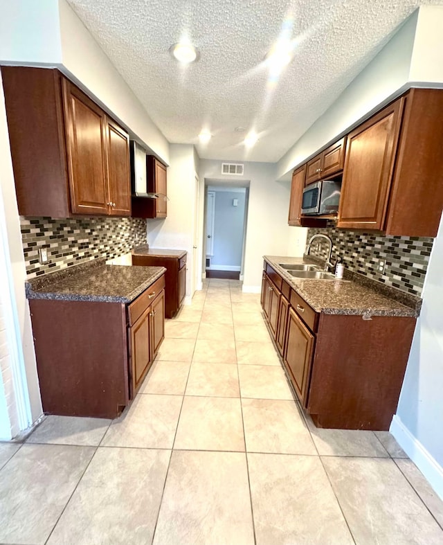 kitchen featuring dark countertops, a sink, stainless steel microwave, and tasteful backsplash