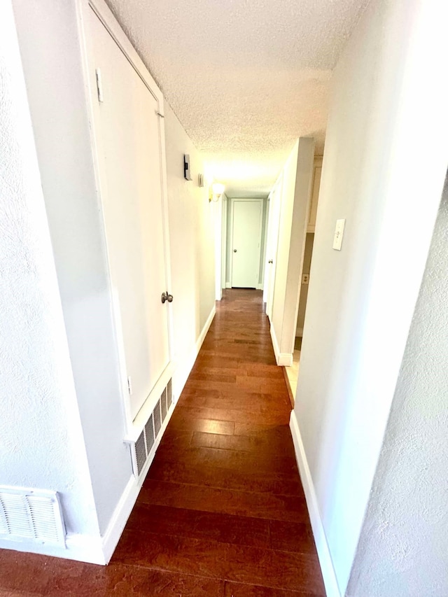 hall featuring baseboards, visible vents, a textured ceiling, and wood-type flooring