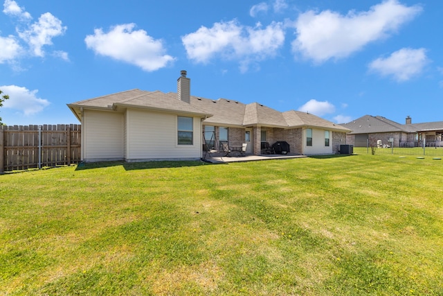 back of property with a fenced backyard, a chimney, a patio area, and a lawn