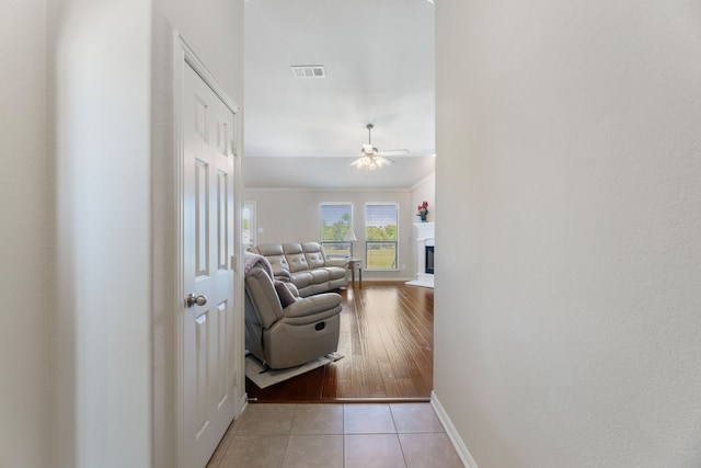 hallway featuring visible vents, crown molding, baseboards, and light tile patterned floors