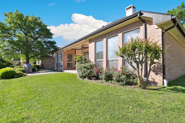 rear view of property featuring a chimney, a patio area, ceiling fan, a lawn, and brick siding