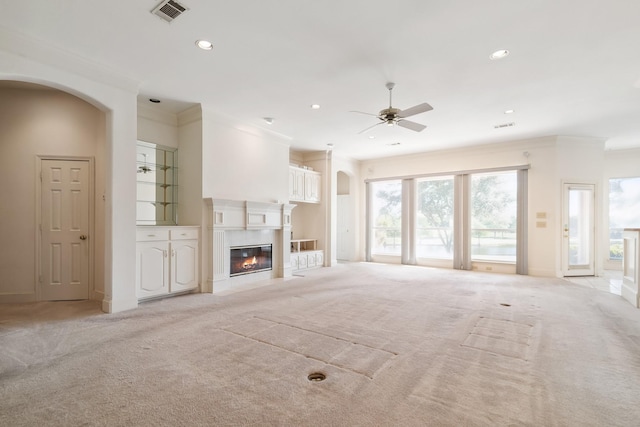 unfurnished living room with visible vents, a ceiling fan, light carpet, arched walkways, and crown molding