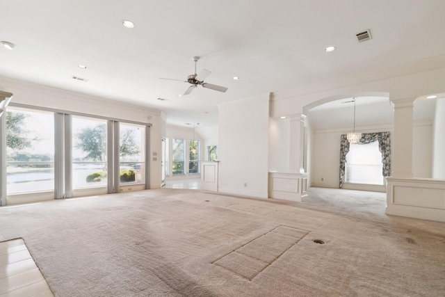 unfurnished living room with arched walkways, decorative columns, light colored carpet, ceiling fan, and crown molding