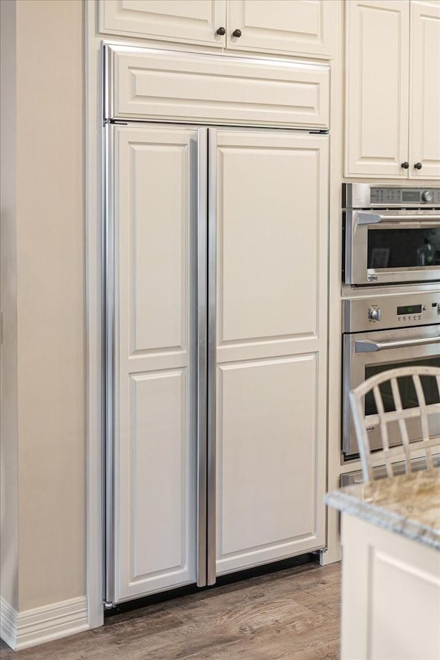 1608 Ridgewood Dr, Waco, TX 76710 - interior space featuring stainless steel double oven, light stone counters, wood finished floors, baseboards, and white cabinetry