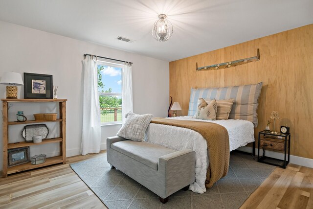 bedroom with a notable chandelier, wood walls, baseboards, wood finished floors, and visible vents