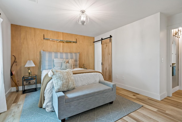 bedroom featuring wooden walls, baseboards, a barn door, and wood finished floors