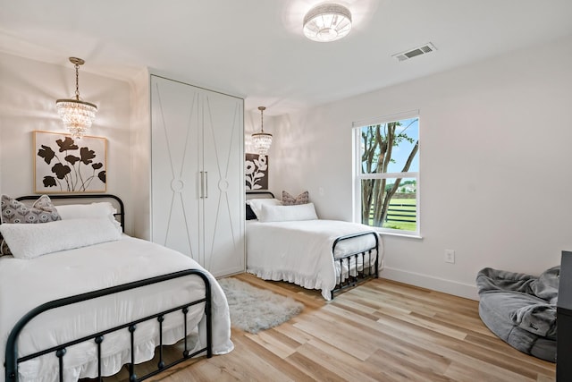 bedroom with wood finished floors, baseboards, a chandelier, and visible vents