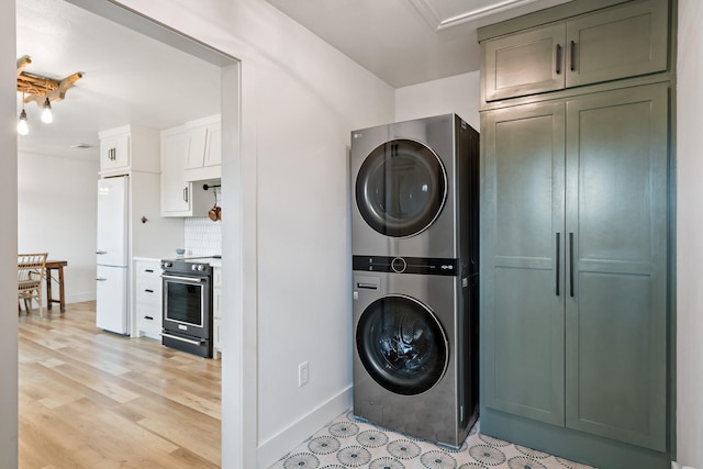 laundry area featuring cabinet space, baseboards, stacked washer and clothes dryer, and light wood-type flooring