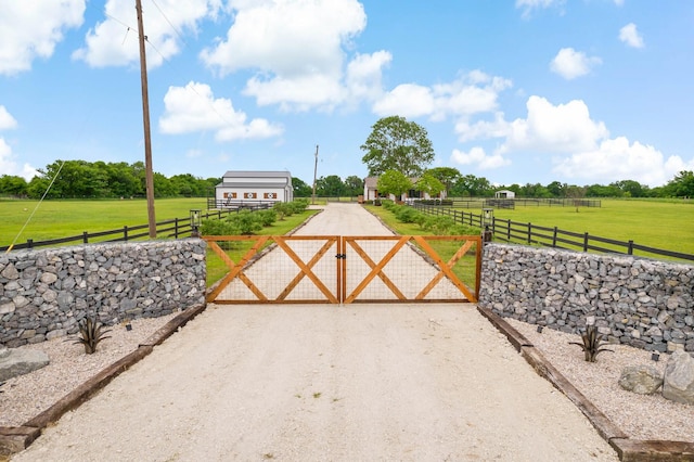view of gate featuring fence, a lawn, and a rural view