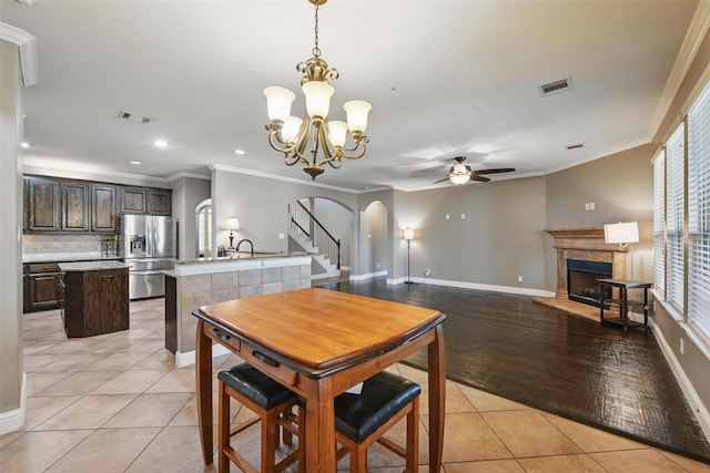 dining space with a tile fireplace, visible vents, arched walkways, light tile patterned flooring, and ceiling fan with notable chandelier