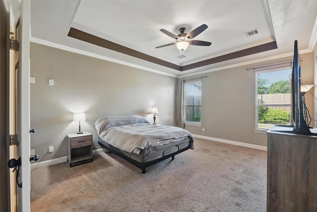 carpeted bedroom with a tray ceiling, visible vents, baseboards, and ornamental molding