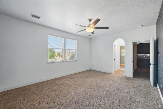 unfurnished bedroom featuring arched walkways, light carpet, multiple windows, and visible vents