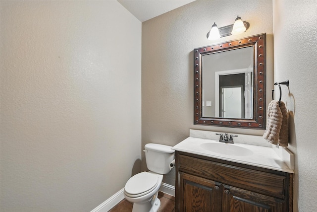 half bath featuring a textured wall, baseboards, vanity, and toilet