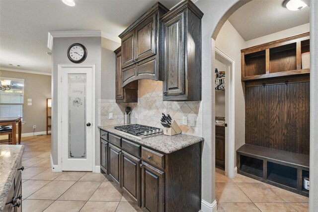 kitchen featuring stainless steel gas stovetop, light tile patterned floors, arched walkways, crown molding, and decorative backsplash