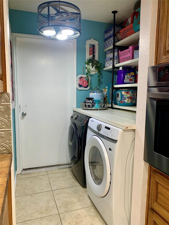laundry room featuring washing machine and clothes dryer, a textured ceiling, laundry area, and light tile patterned floors