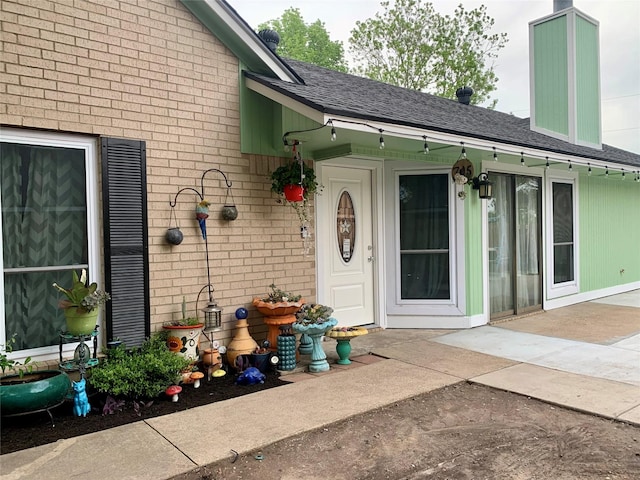 property entrance with a chimney, brick siding, and roof with shingles