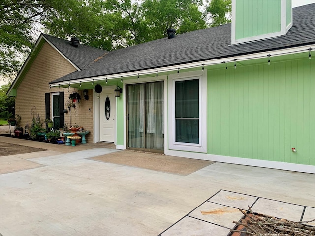 back of property with brick siding, a patio area, and roof with shingles