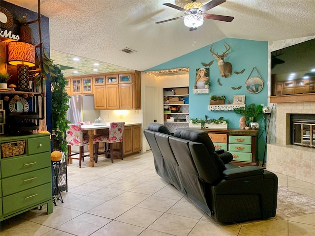 living room featuring vaulted ceiling, a textured ceiling, light tile patterned floors, ceiling fan, and visible vents